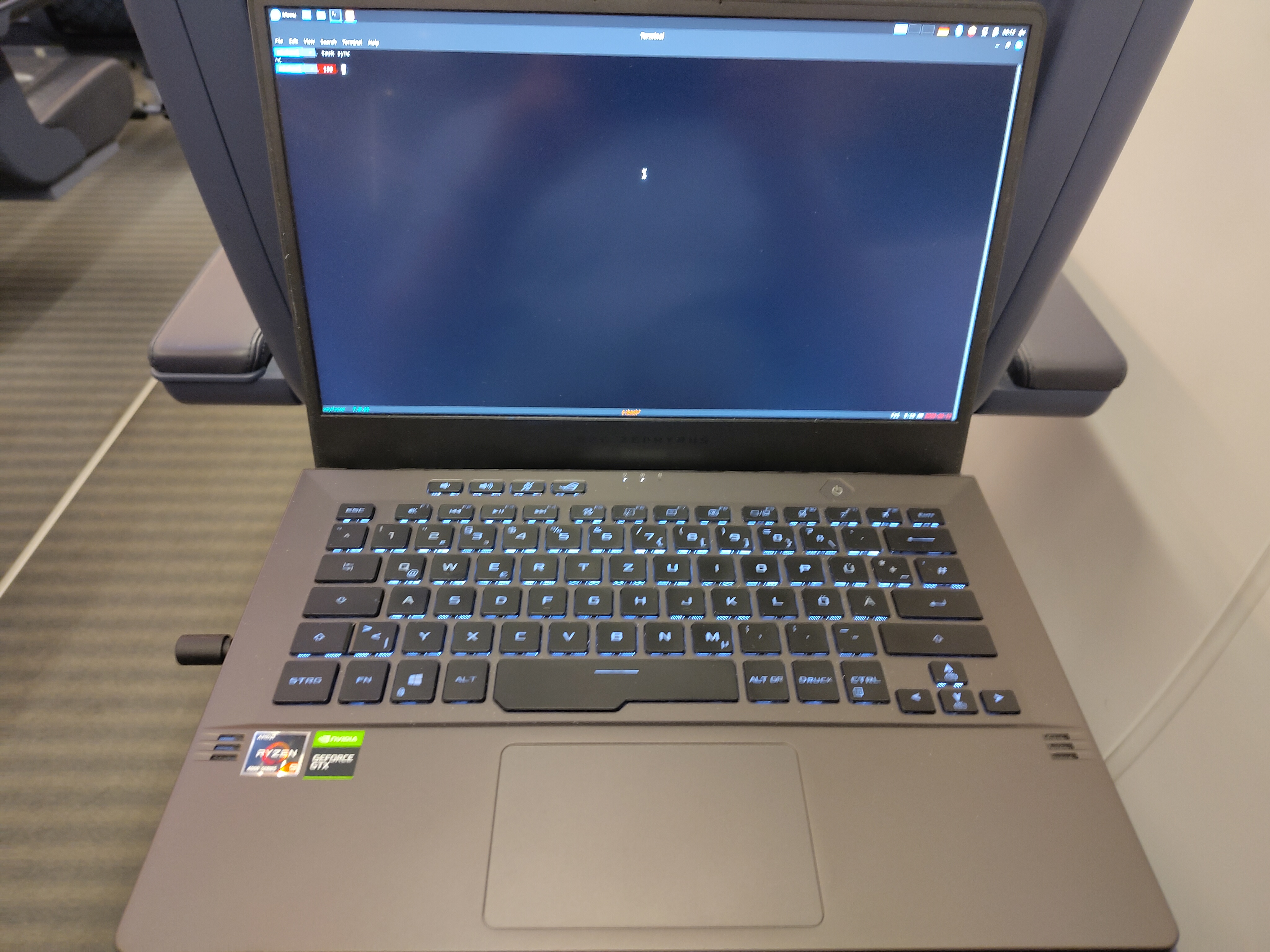 A picture of a gamery Asus laptop resting on the tray of a Deutsche Bahn ICE first class seat. It has an empty terminal window open, just showing the prompt with the username 'michael'.