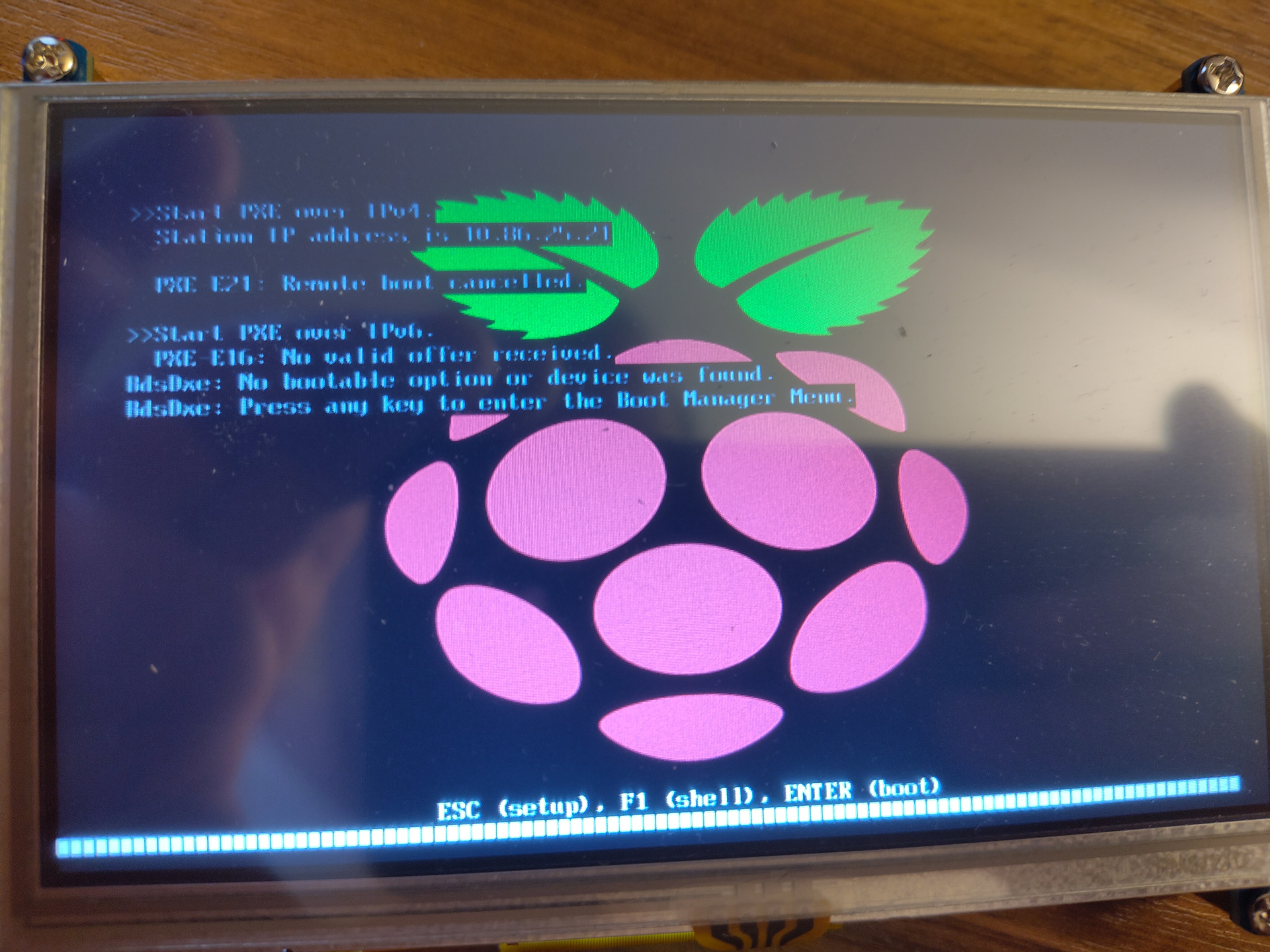 A picture of a screen showing the Pi booted into the UEFI firmware. In the background, it shows the Raspberry Pi raspberry. At the bottom, several shortcuts are shown to enter setup, the shell or continue booting. At the top, text showing an attempt to do a PXE boot via IPv4 and IPv6 is displayed. In both cases, the remote boot failed.