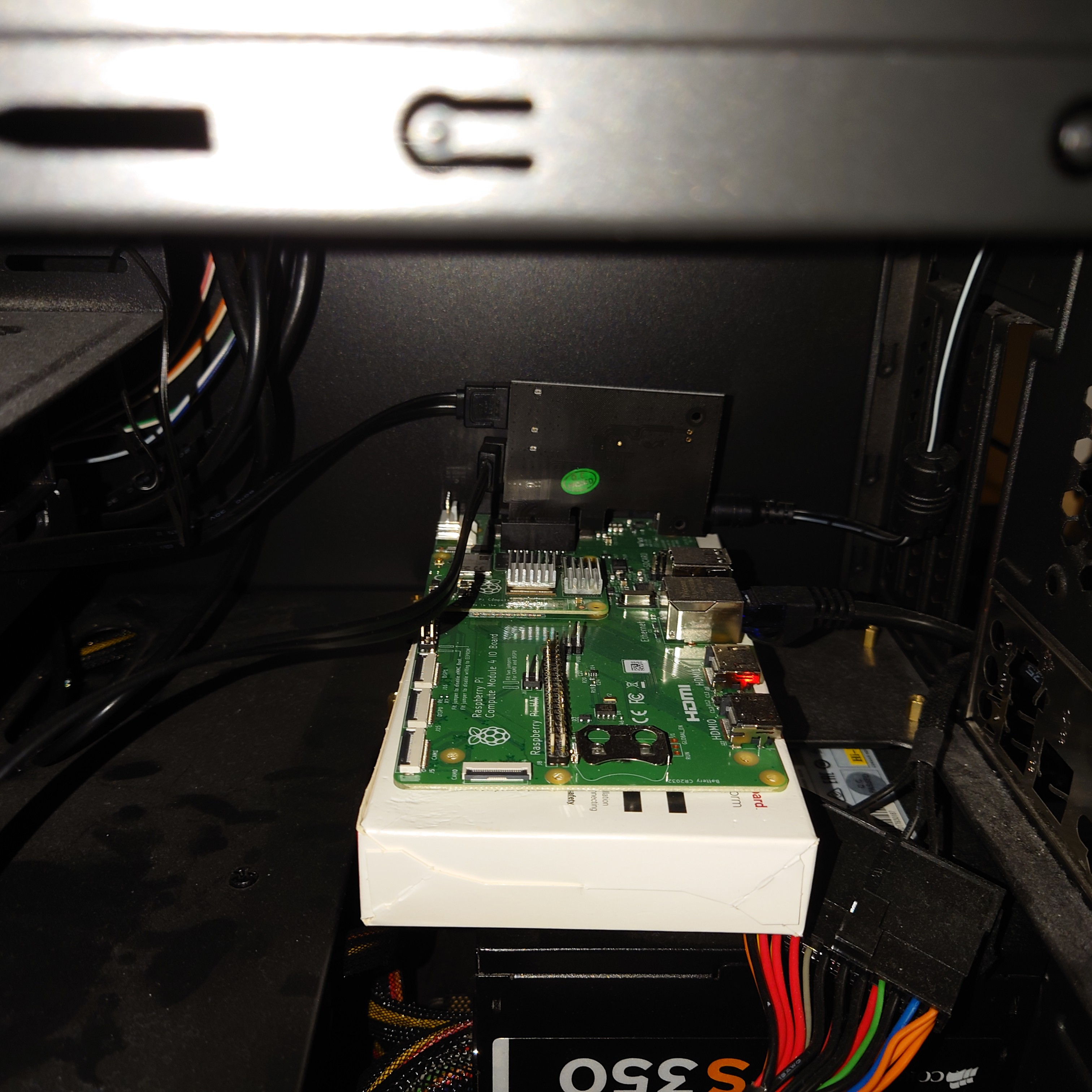 A picture of a CM4 IO board, with a CM4 attached. The IO board sits in a PC case, not fastened anywhere, resting on the cardboard box the IO board came in. A SATA card is attached to the IO board's PCIe slot, with two SATA cables connected to it.