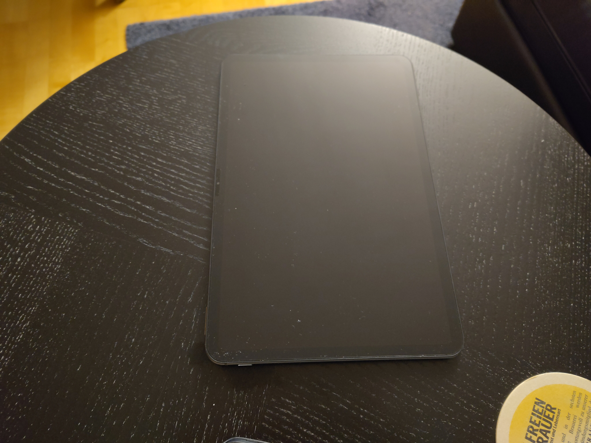 A picture of the Volla tablet from the front, with the screen facing the camera. It's sitting flat on a black table. The display is 12 inches in size, surrounded on all sides by a black bezel. On the right, long side, it has an integrated webcam. On the top-right is a button. There's literally nothing else I could write. It's basically looking like any other of the thousands of Android tablets.